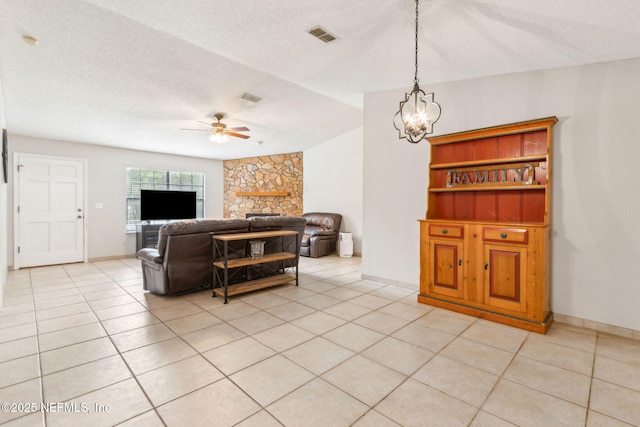 living room featuring a ceiling fan, a textured ceiling, light tile patterned floors, a fireplace, and a chandelier