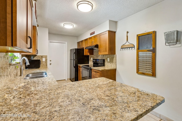kitchen with black appliances, a sink, under cabinet range hood, brown cabinetry, and backsplash