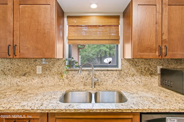 kitchen with a sink, light stone counters, backsplash, brown cabinets, and stainless steel dishwasher
