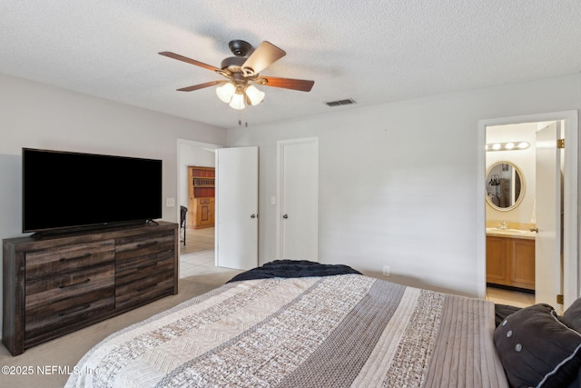 bedroom with a sink, ceiling fan, a textured ceiling, ensuite bath, and light colored carpet
