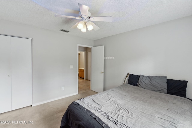 bedroom featuring light carpet, a closet, a textured ceiling, a ceiling fan, and baseboards