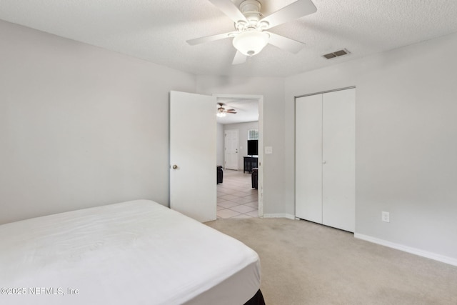 bedroom with light carpet, a closet, ceiling fan, baseboards, and a textured ceiling
