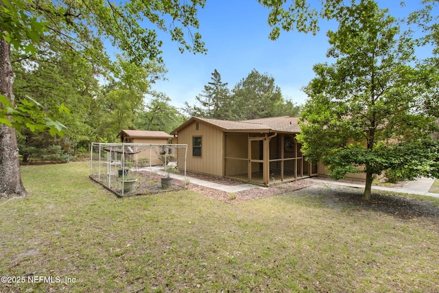back of property with a garden, a yard, a sunroom, and a shingled roof