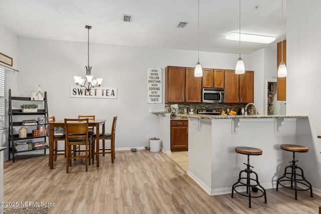607 Golden Lake Loop, Saint Augustine, FL 32084 - kitchen featuring stainless steel appliances, brown cabinetry, a breakfast bar, light wood finished floors, and light stone countertops