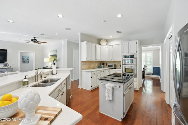 kitchen featuring appliances with stainless steel finishes, a sink, a center island, tasteful backsplash, and white cabinets