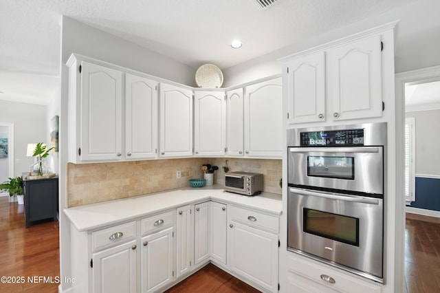 kitchen featuring stainless steel double oven, backsplash, white cabinets, dark wood-type flooring, and recessed lighting