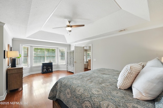 bedroom with a tray ceiling, wood finished floors, baseboards, ornamental molding, and ceiling fan