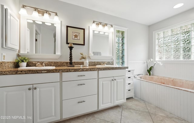 full bath with wainscoting, double vanity, a bath, and tile patterned floors