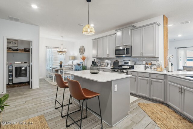 kitchen with appliances with stainless steel finishes, gray cabinetry, washer / clothes dryer, backsplash, and light countertops