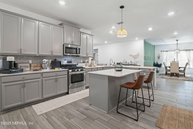 kitchen featuring appliances with stainless steel finishes, gray cabinets, a sink, a peninsula, and a kitchen breakfast bar