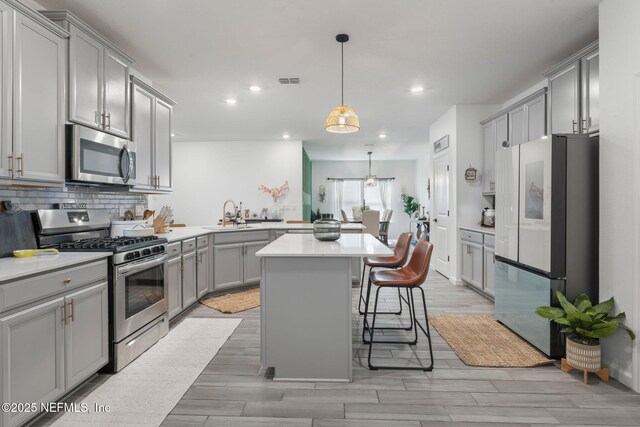kitchen featuring stainless steel appliances, gray cabinets, light countertops, a kitchen breakfast bar, and recessed lighting