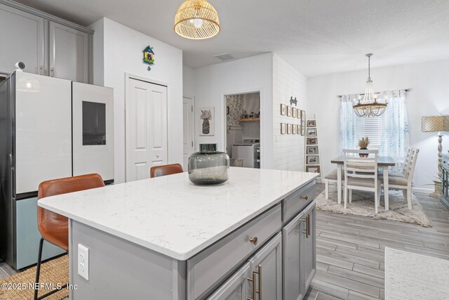 kitchen featuring gray cabinets, freestanding refrigerator, washer / dryer, and a chandelier