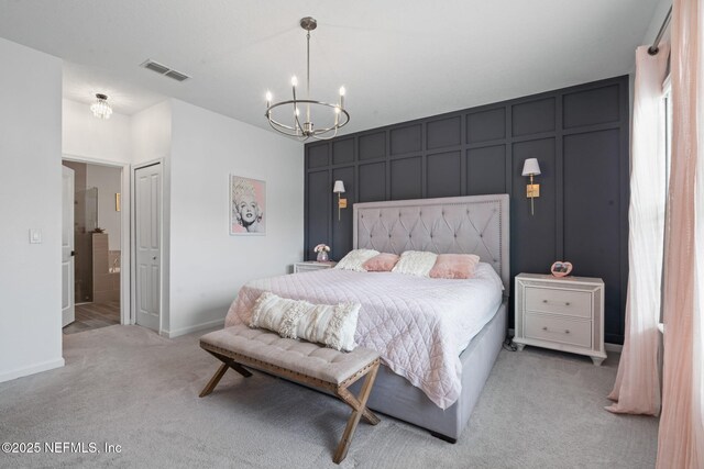 bedroom featuring a chandelier, light colored carpet, a decorative wall, baseboards, and ensuite bathroom