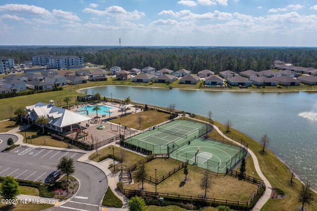 drone / aerial view of a pool area, a large body of water, and a heavily wooded area