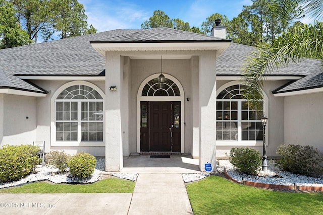 11658 Jerry Adam Ct, Jacksonville, FL 32218 - view of exterior entry featuring a shingled roof, a chimney, and stucco siding