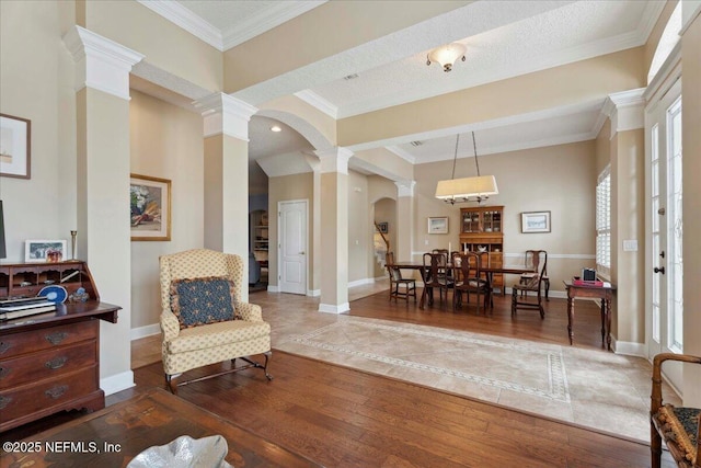 living area with decorative columns, arched walkways, wood finished floors, baseboards, and crown molding