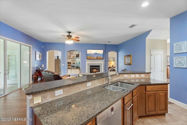 kitchen featuring open floor plan, arched walkways, stainless steel dishwasher, a sink, and brown cabinets