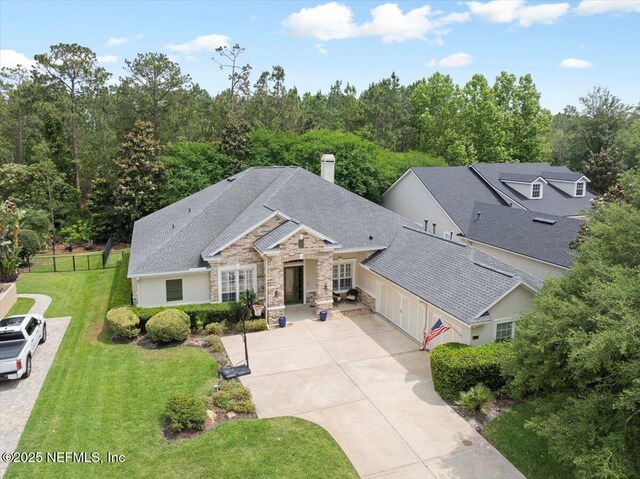 view of front of property with stone siding, a garage, driveway, a chimney, and a shingled roof