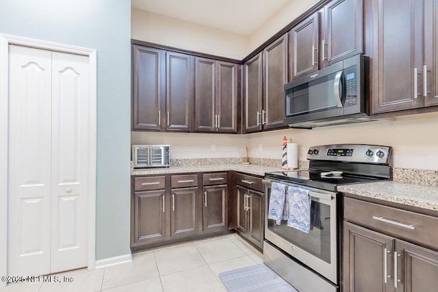 kitchen with appliances with stainless steel finishes, dark brown cabinets, light tile patterned floors, and light stone counters