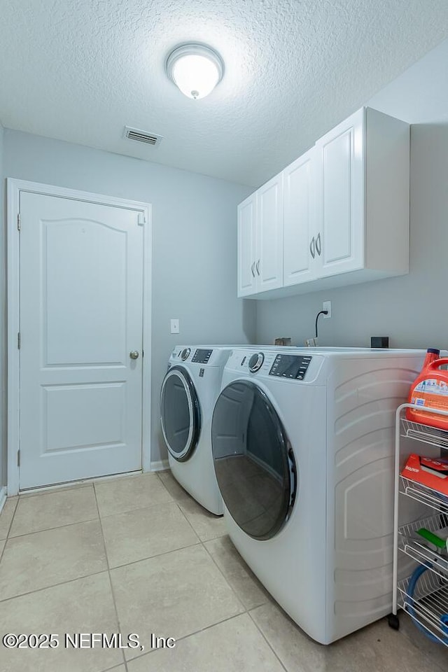 laundry area with cabinet space, a textured ceiling, washer and clothes dryer, and light tile patterned floors