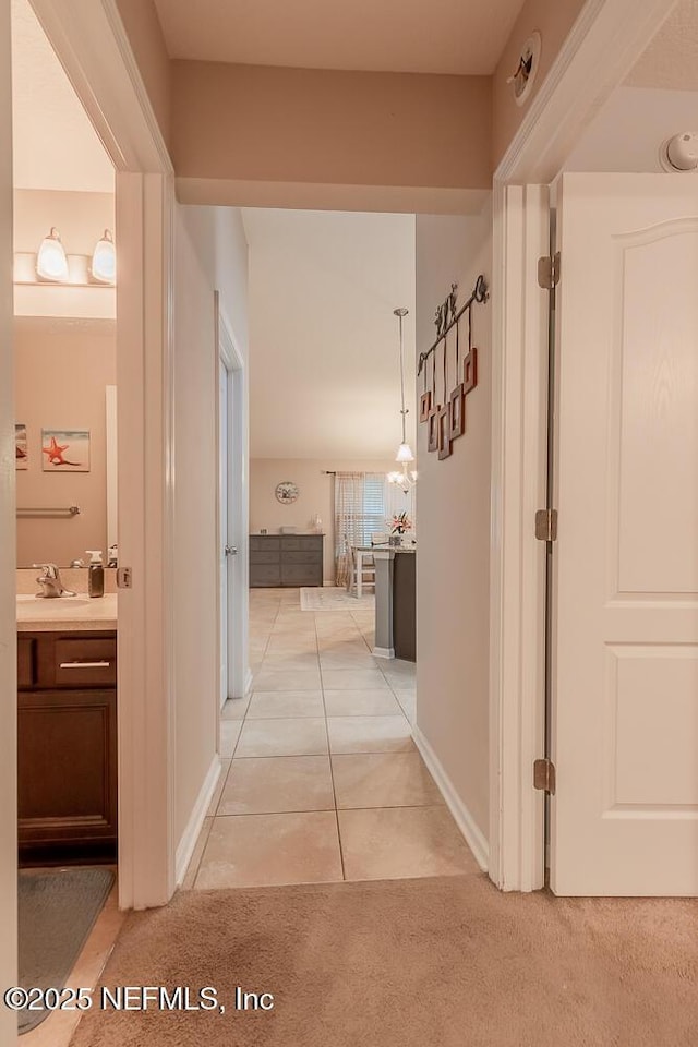 hall with light tile patterned floors, a sink, and light colored carpet