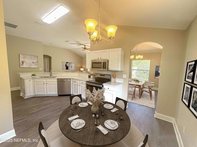 dining room featuring a chandelier, arched walkways, baseboards, ceiling fan, and vaulted ceiling