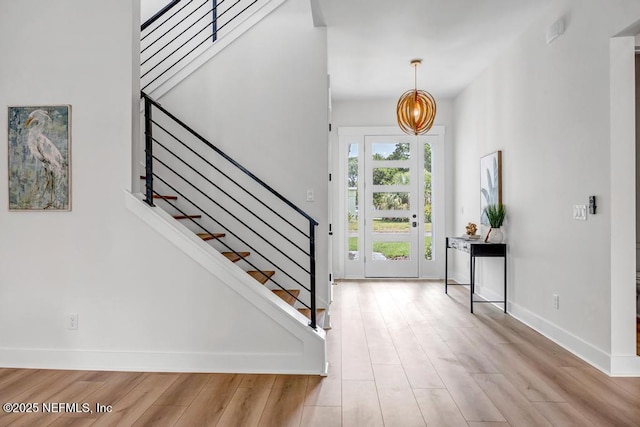 foyer featuring wood finished floors, stairway, baseboards, and a chandelier