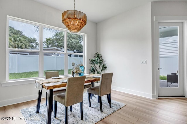 dining space with light wood finished floors, healthy amount of natural light, a chandelier, and baseboards