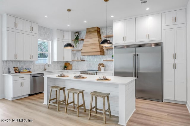 kitchen featuring stainless steel appliances, custom exhaust hood, open shelves, a sink, and light countertops