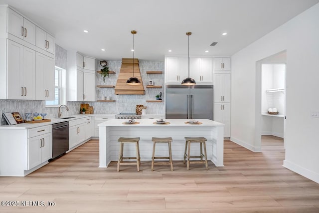kitchen with appliances with stainless steel finishes, open shelves, custom range hood, a kitchen breakfast bar, and a center island
