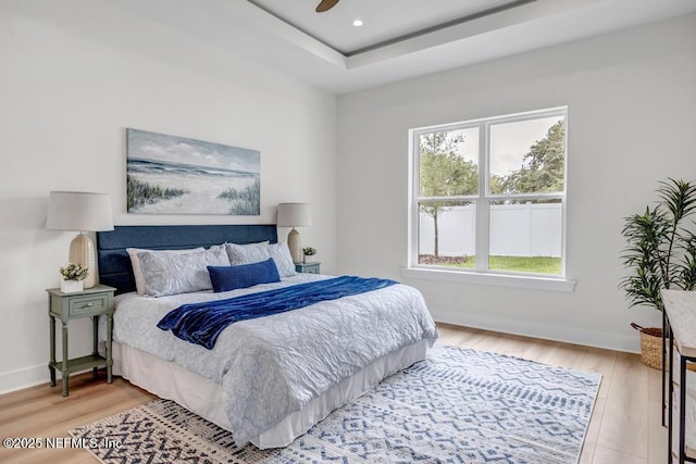 bedroom with light wood-style flooring, baseboards, a tray ceiling, and recessed lighting