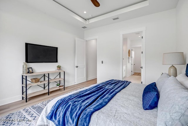 bedroom with wood finished floors, a raised ceiling, baseboards, and a ceiling fan