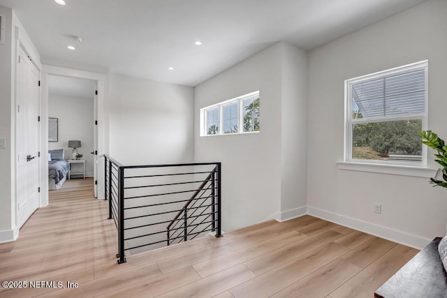 hallway with an upstairs landing, plenty of natural light, wood finished floors, recessed lighting, and baseboards