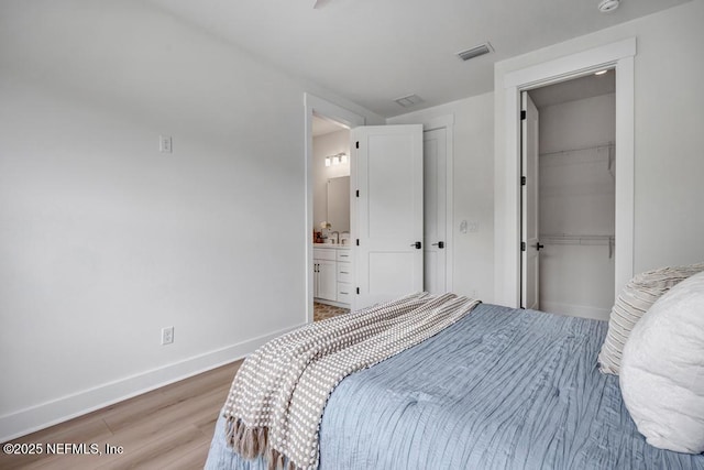 bedroom with light wood-style floors, baseboards, a closet, ensuite bathroom, and a walk in closet