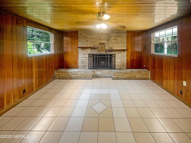 unfurnished living room featuring wooden ceiling, a ceiling fan, wooden walls, a fireplace, and tile patterned floors