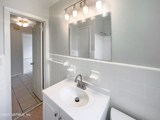 bathroom with toilet, vanity, a wainscoted wall, tile walls, and tile patterned floors