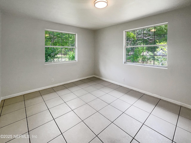 empty room featuring healthy amount of natural light, light tile patterned floors, and baseboards