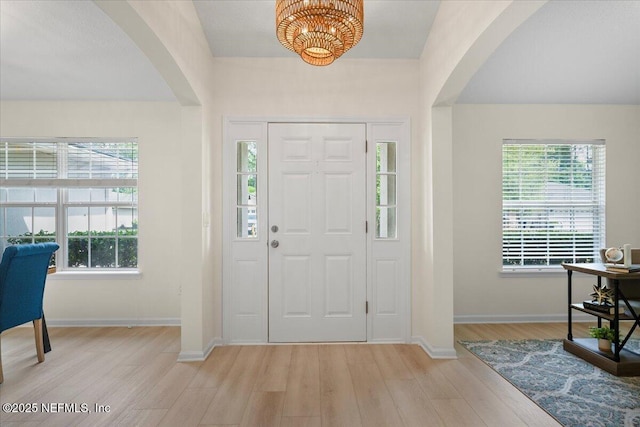 entryway featuring arched walkways, light wood-type flooring, and baseboards