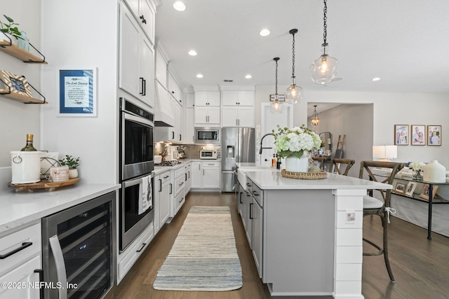 kitchen featuring wine cooler, appliances with stainless steel finishes, a kitchen breakfast bar, an island with sink, and dark wood-style floors