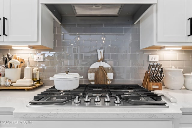 kitchen view of stainless steel gas cooktop, decorative backsplash, white cabinets, custom range hood, and light stone countertops