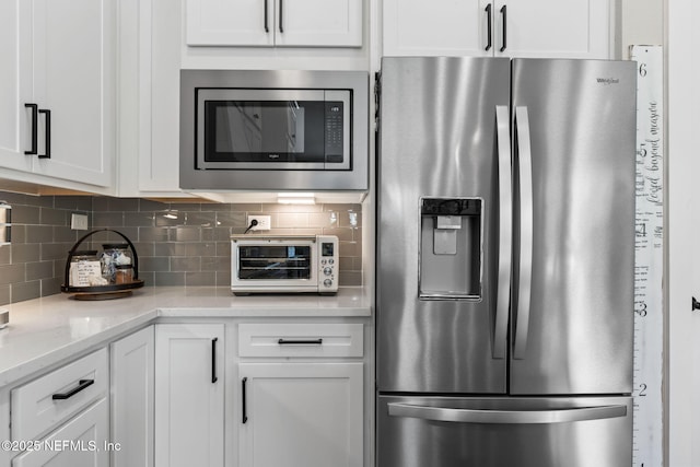 kitchen with stainless steel appliances, white cabinetry, tasteful backsplash, and light stone counters