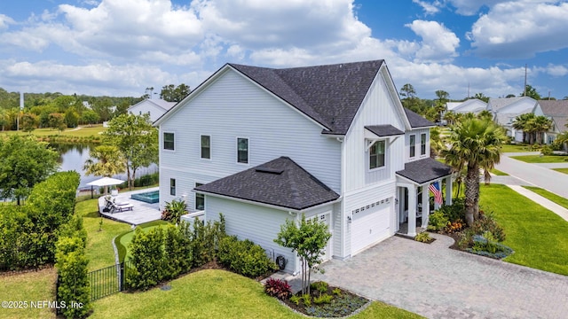 view of side of property featuring roof with shingles, a garage, driveway, board and batten siding, and a water view