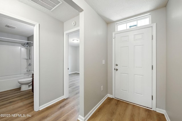 entryway featuring light wood-type flooring, a textured ceiling, and baseboards