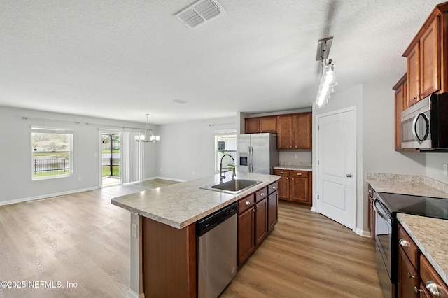 kitchen with stainless steel appliances, a sink, light wood finished floors, a chandelier, and a textured ceiling
