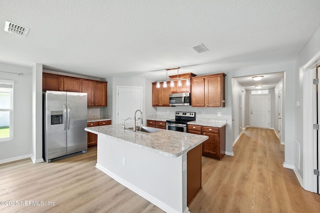 kitchen with appliances with stainless steel finishes, a sink, light wood finished floors, light countertops, and brown cabinetry