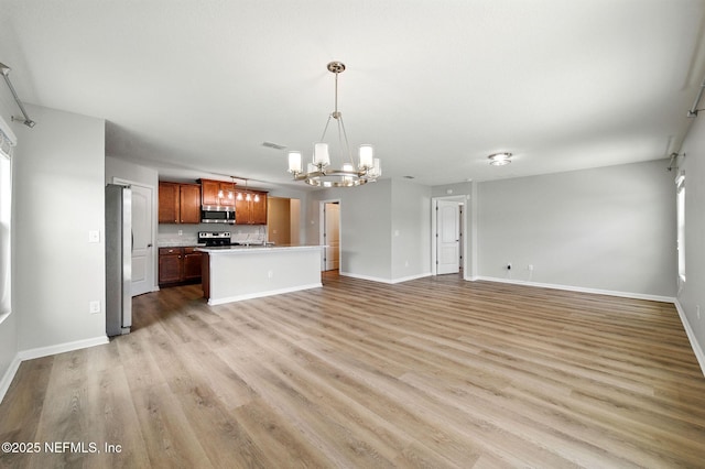 unfurnished living room with a chandelier, light wood finished floors, baseboards, and a sink