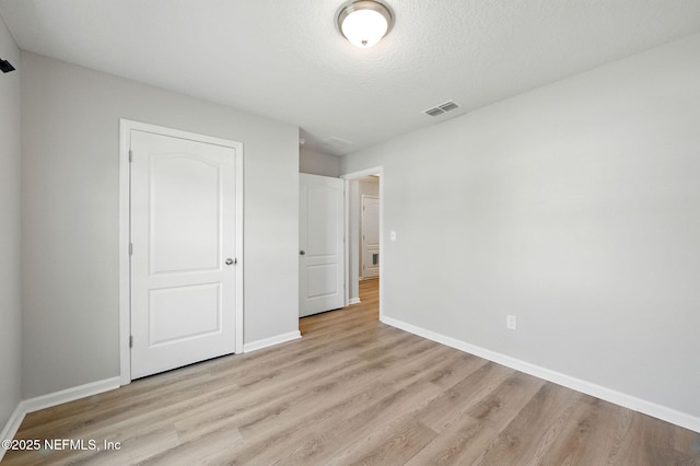 unfurnished bedroom featuring light wood-type flooring, baseboards, and a textured ceiling
