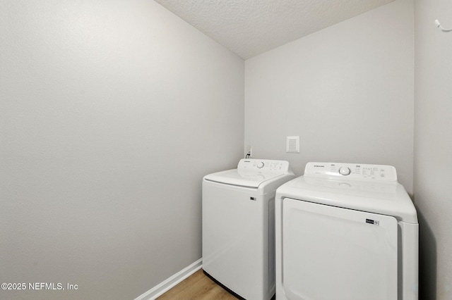 laundry room with washer and clothes dryer, a textured ceiling, light wood finished floors, and baseboards