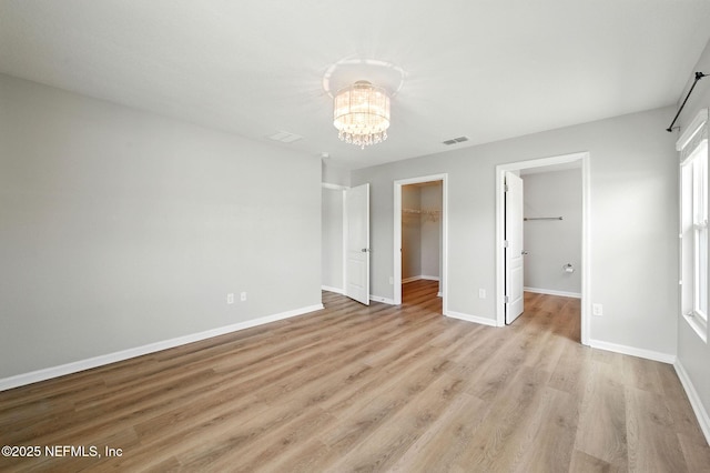 unfurnished bedroom featuring a chandelier, a walk in closet, light wood finished floors, baseboards, and a closet