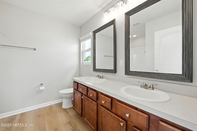 full bathroom featuring double vanity, wood finished floors, toilet, and baseboards